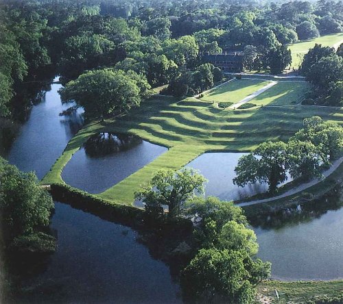 Aerial view of a lush green landscape with a winding river and manicured lawns surrounded by trees.