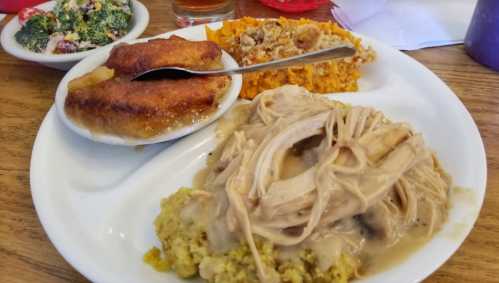 A plate of food featuring shredded chicken with gravy, stuffing, sweet potato casserole, and cornbread.