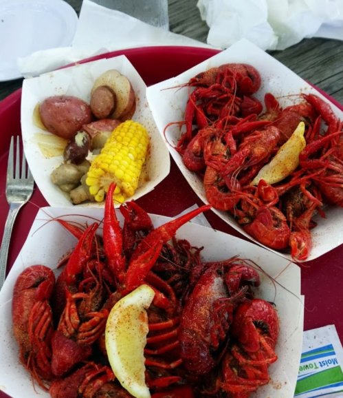 A red tray with three servings of seasoned crawfish, potatoes, corn, and lemon slices.