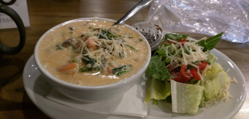 A bowl of creamy soup with vegetables and cheese, served alongside a fresh salad with lettuce and tomatoes.