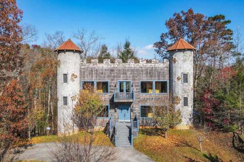 A castle-like house with turrets, surrounded by trees and autumn foliage, under a clear blue sky.