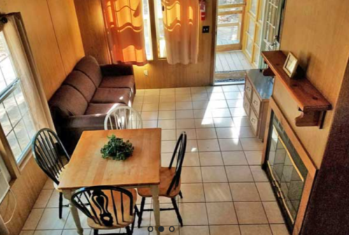 Cozy interior of a cabin featuring a sofa, dining table, and large windows with natural light.
