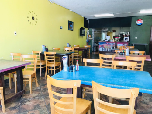 A colorful, empty restaurant interior with wooden tables and chairs, featuring a counter in the background.