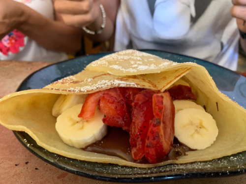 A delicious crepe filled with strawberries, bananas, and chocolate sauce, served on a blue plate.