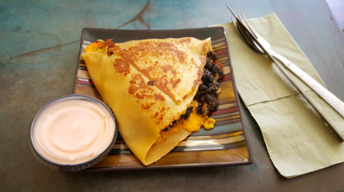 A savory crepe filled with black beans and cheese, served with a side of dipping sauce on a colorful plate.