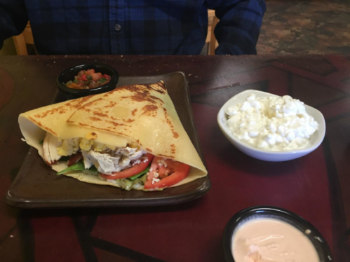 A plate with a folded crepe filled with chicken, lettuce, and tomato, alongside a bowl of cottage cheese and salsa.