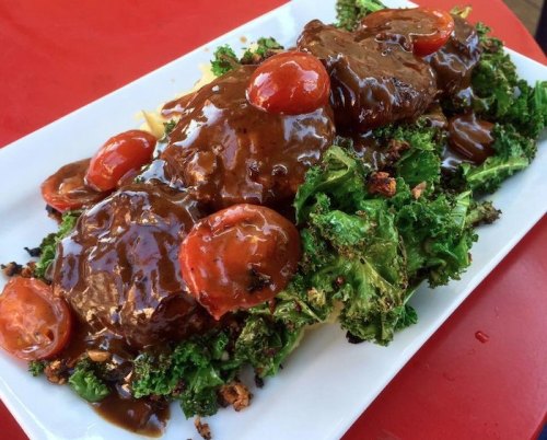 A plate of meatloaf topped with gravy and cherry tomatoes, served on a bed of sautéed kale.