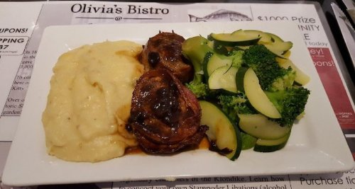 A plate featuring mashed potatoes, two meat portions with sauce, and a side of steamed broccoli and zucchini.