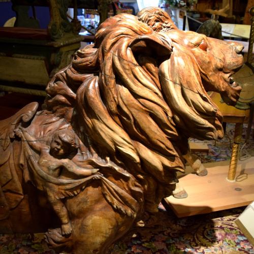 A detailed wooden sculpture of a lion with a small figure of a child riding on its back, showcasing intricate craftsmanship.