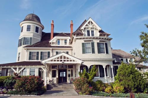 A large, elegant Victorian-style house with a turret, surrounded by lush greenery and colorful flowers.