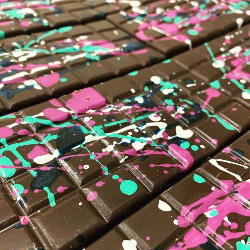 Close-up of chocolate bars with colorful splatters of pink, turquoise, and black paint on the surface.