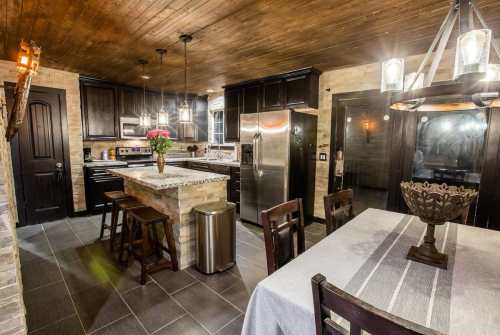 Modern kitchen with dark cabinets, granite countertops, and a dining table, featuring pendant lights and a rustic ceiling.