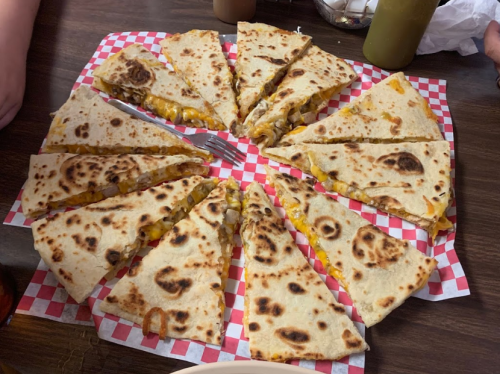 A large platter of sliced quesadillas with melted cheese and fillings, arranged in a circular pattern on a checkered paper.