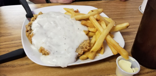 A plate of fried chicken smothered in white gravy, served with French fries and a small cup of butter.