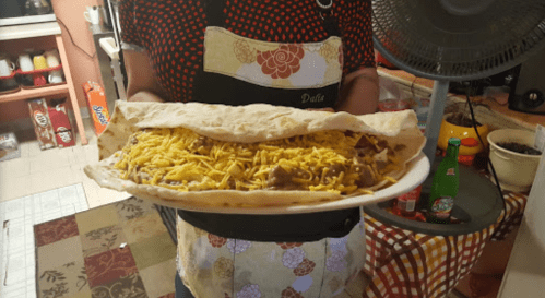 A person holds a large plate with a stuffed tortilla filled with beans and topped with shredded cheese.