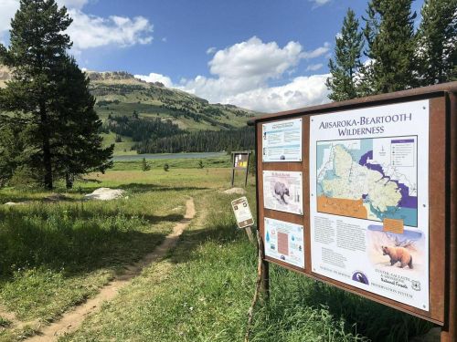 Sign for Absaroka-Beartooth Wilderness with a scenic view of mountains and a grassy trail in the background.