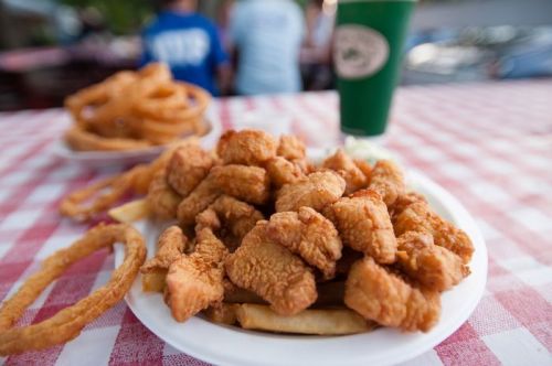 A plate of crispy fried chicken pieces served with fries and onion rings, set on a checkered tablecloth.
