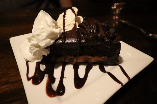 A slice of rich chocolate cake topped with whipped cream and drizzled with chocolate sauce on a white plate.