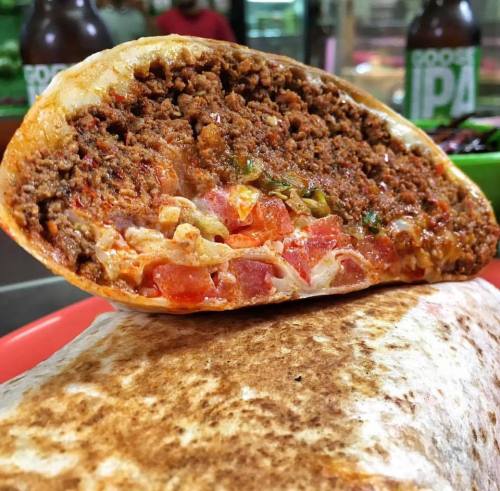 A close-up of a cut burrito filled with seasoned meat, tomatoes, and peppers, resting on a plate.