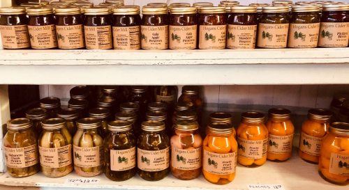 A shelf filled with jars of various preserves and pickles, labeled with "Higgins Cider Mill" and prices.