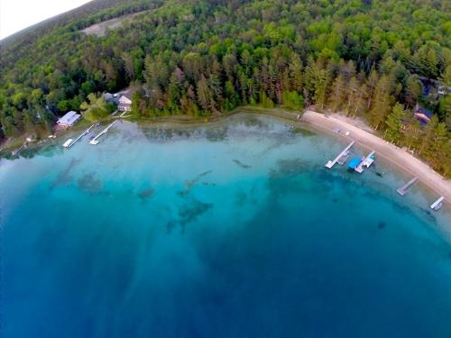 Aerial view of a serene lake with clear blue water, sandy beach, and lush green trees along the shoreline.