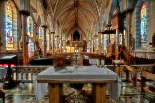 Interior of a grand church featuring stained glass windows, a central altar, and ornate architectural details.