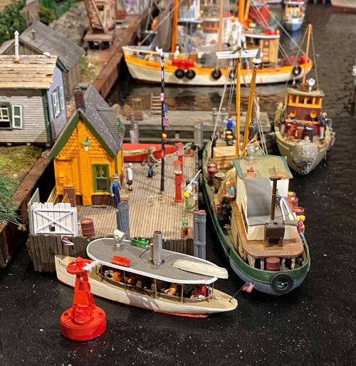 A miniature harbor scene with boats, a dock, and small figures, showcasing detailed model craftsmanship.
