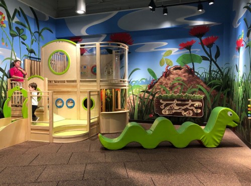A colorful children's play area featuring a wooden structure and a green caterpillar toy against a vibrant mural.