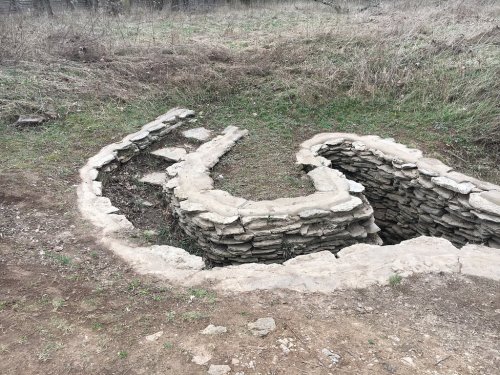A curved stone structure partially buried in grass, resembling a trench or old foundation in a natural setting.