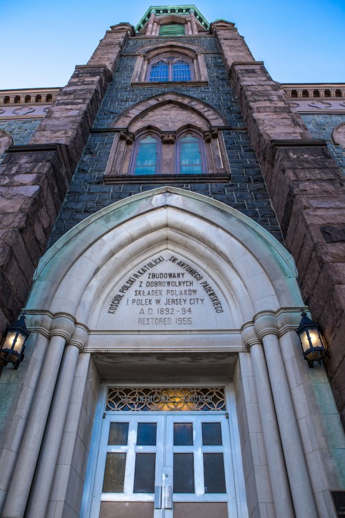 Facade of a historic church with ornate stonework and a large entrance, featuring a date of restoration in 1955.