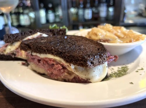 A close-up of a corned beef sandwich on rye bread, served with a side of macaroni and cheese.