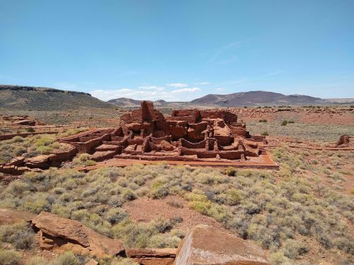 Ancient red stone ruins surrounded by desert landscape and mountains under a clear blue sky.