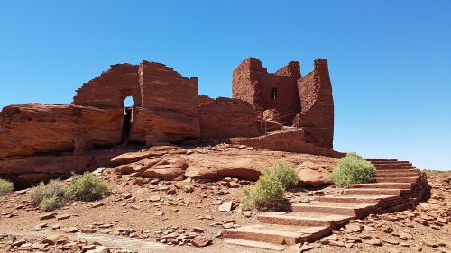 Ancient stone ruins on a rocky landscape under a clear blue sky, with steps leading up to the structure.