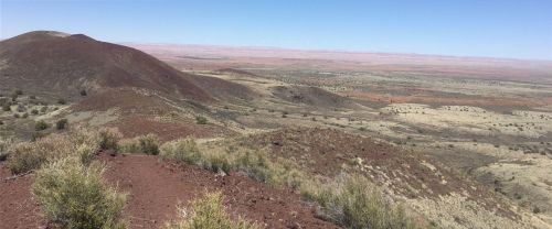 A panoramic view of a rugged landscape with red hills and sparse vegetation under a clear blue sky.