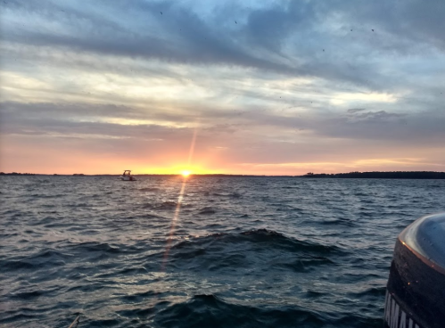 A serene sunset over the water, with gentle waves and a small boat in the distance.
