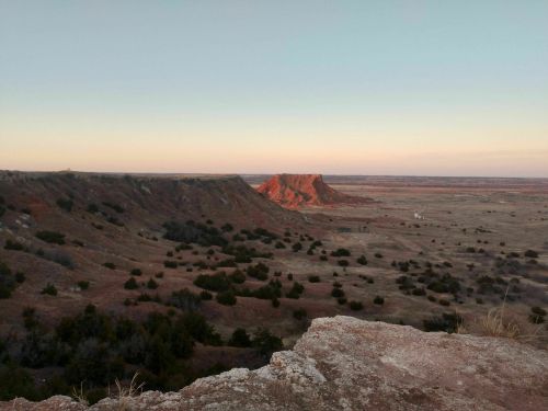 A panoramic view of a rugged landscape with red rock formations and rolling hills under a clear sky.