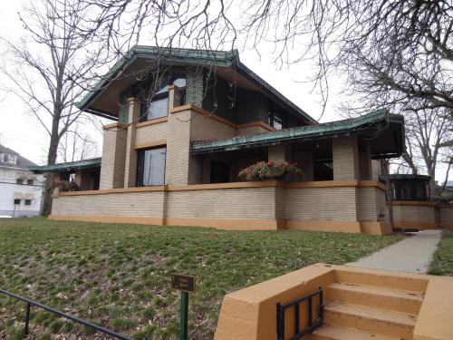 A large, two-story house with a green roof, brick exterior, and flower boxes, surrounded by bare trees and grass.