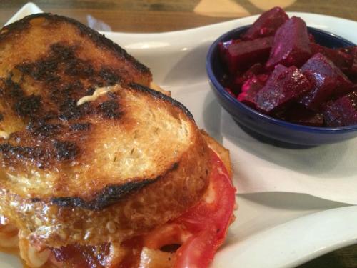 A grilled cheese sandwich with crispy bread, served with a side of diced roasted beets in a small bowl.