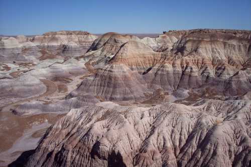 A vast landscape of colorful, layered hills and valleys under a clear blue sky, showcasing natural geological formations.