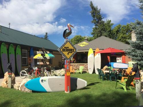A vibrant outdoor area with surfboards, bicycles, colorful chairs, and a signpost, surrounded by trees and a blue sky.