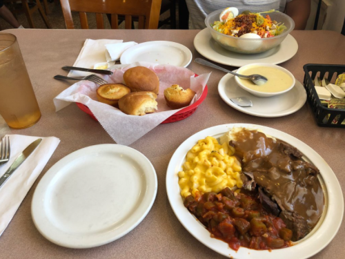 A table with two plates of food: one with macaroni and cheese, beef, and chili; the other with a salad and cornbread.