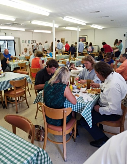 A busy restaurant interior with patrons dining at tables covered in green checkered tablecloths.