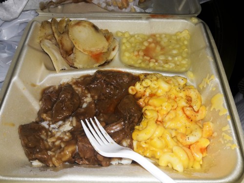 A takeout container with rice, beef stew, macaroni and cheese, and potato wedges.