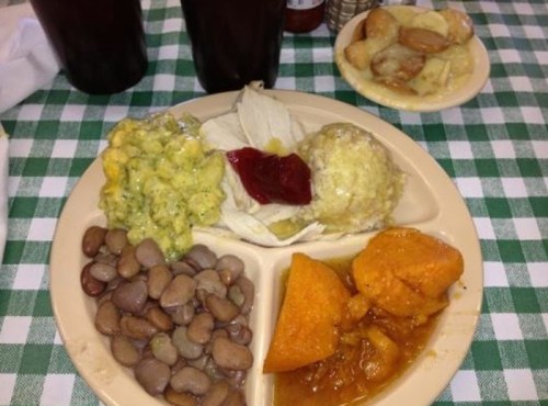 A divided plate with macaroni, chicken with ketchup, sweet potatoes, and beans, alongside a side of fried potatoes.