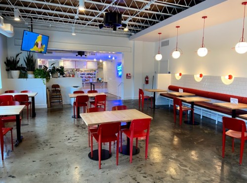 Bright, modern restaurant interior with red chairs, wooden tables, and a TV, featuring a clean, minimalist design.