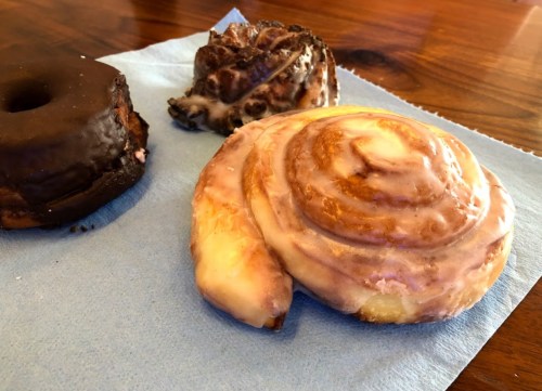 A glazed cinnamon roll, a chocolate donut, and a pastry with chocolate icing on a blue napkin.