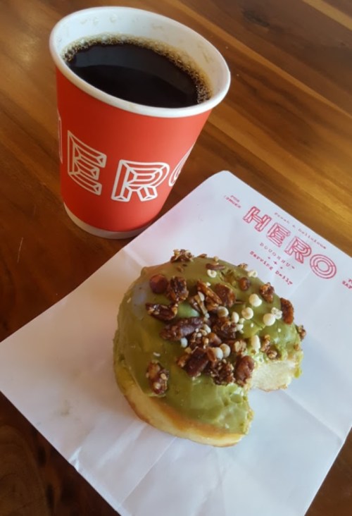 A coffee cup next to a donut topped with green icing and nuts, resting on a branded paper napkin.