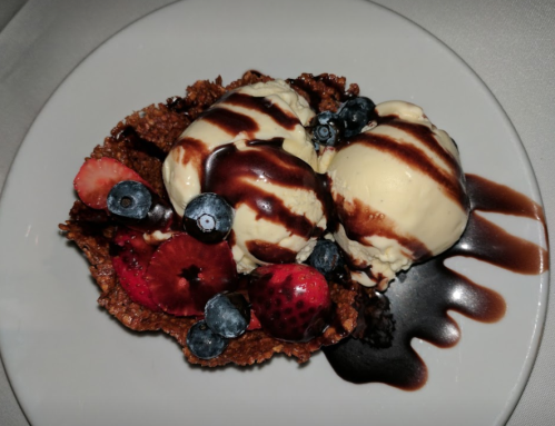A dessert bowl with two scoops of vanilla ice cream, topped with chocolate sauce and mixed berries.