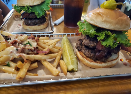 A juicy burger topped with lettuce, bacon, and a pickle, served with fries and a side of creamy sauce.