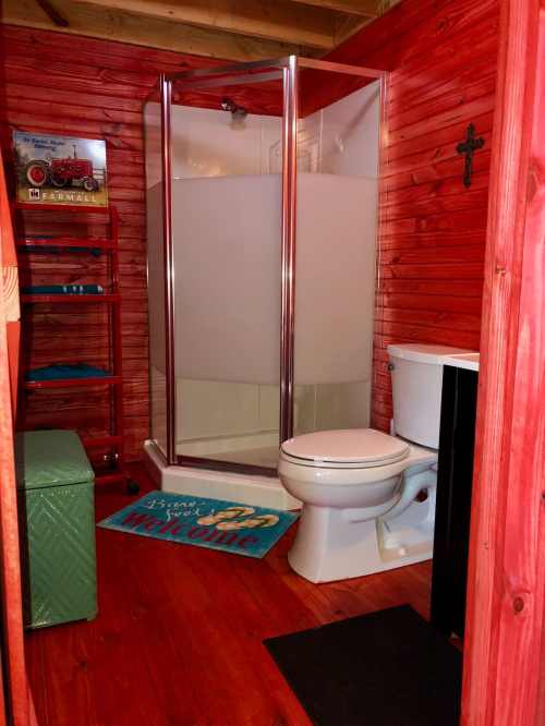 Cozy bathroom with a shower, toilet, and wooden accents, featuring a welcome mat and a vintage decor piece.